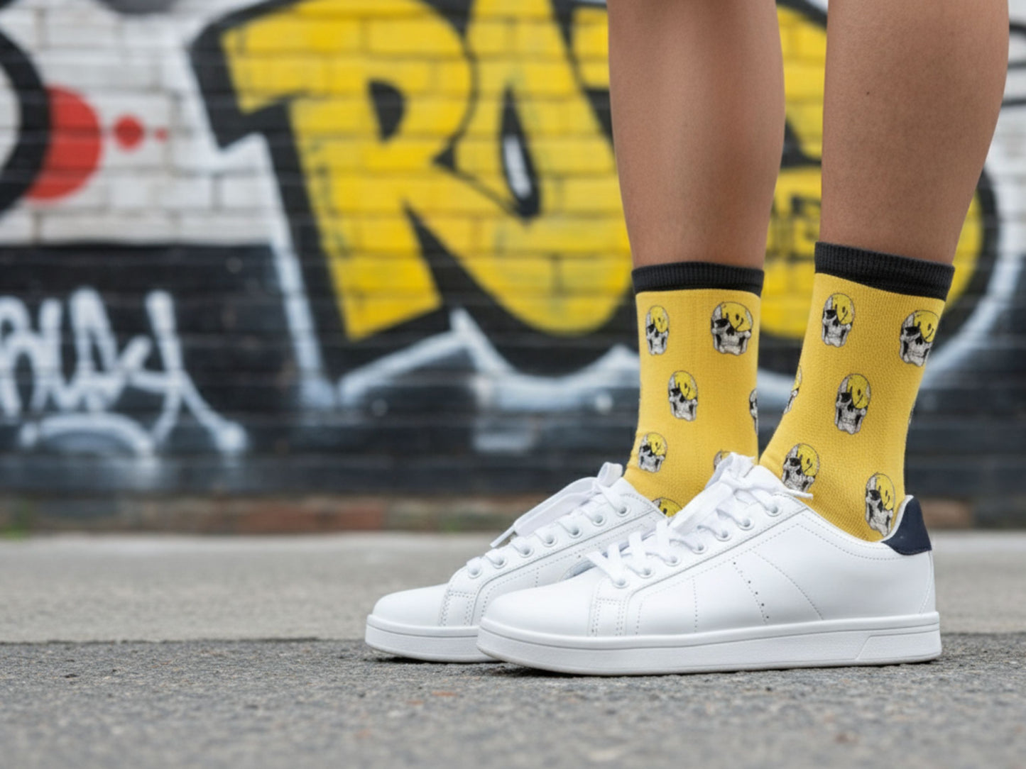 White sneakers with yellow socks featuring black patterns on a street with graffiti.