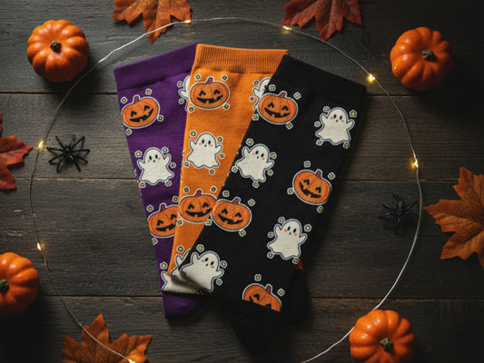 Three Halloween-themed socks with pumpkins and ghosts on a wooden surface with pumpkins and leaves.